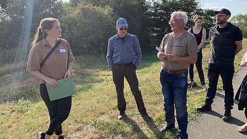 Maria Lindow, Jan Schormann und weitere Teilnehmende stehen auf einer Wiese und sprechen miteinander.