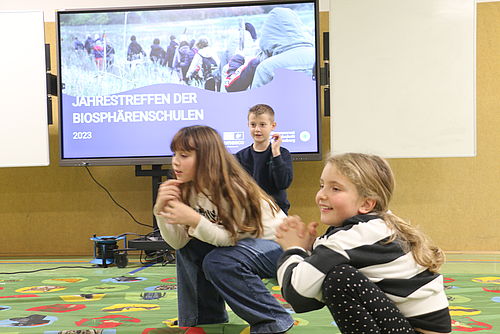 Drei Kinder spielen ein Spiel auf einem farbigen Teppich