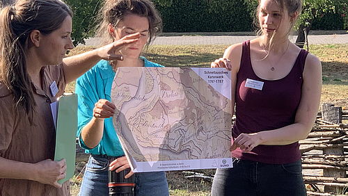  Maria Lindow und zwei weitere Teilnehmerinnen stehen im Freien vor einer Karte zum Projektgebiet.