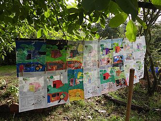 Von Kindern gemalte Bilder hängen auf einer Leine im Garten.
